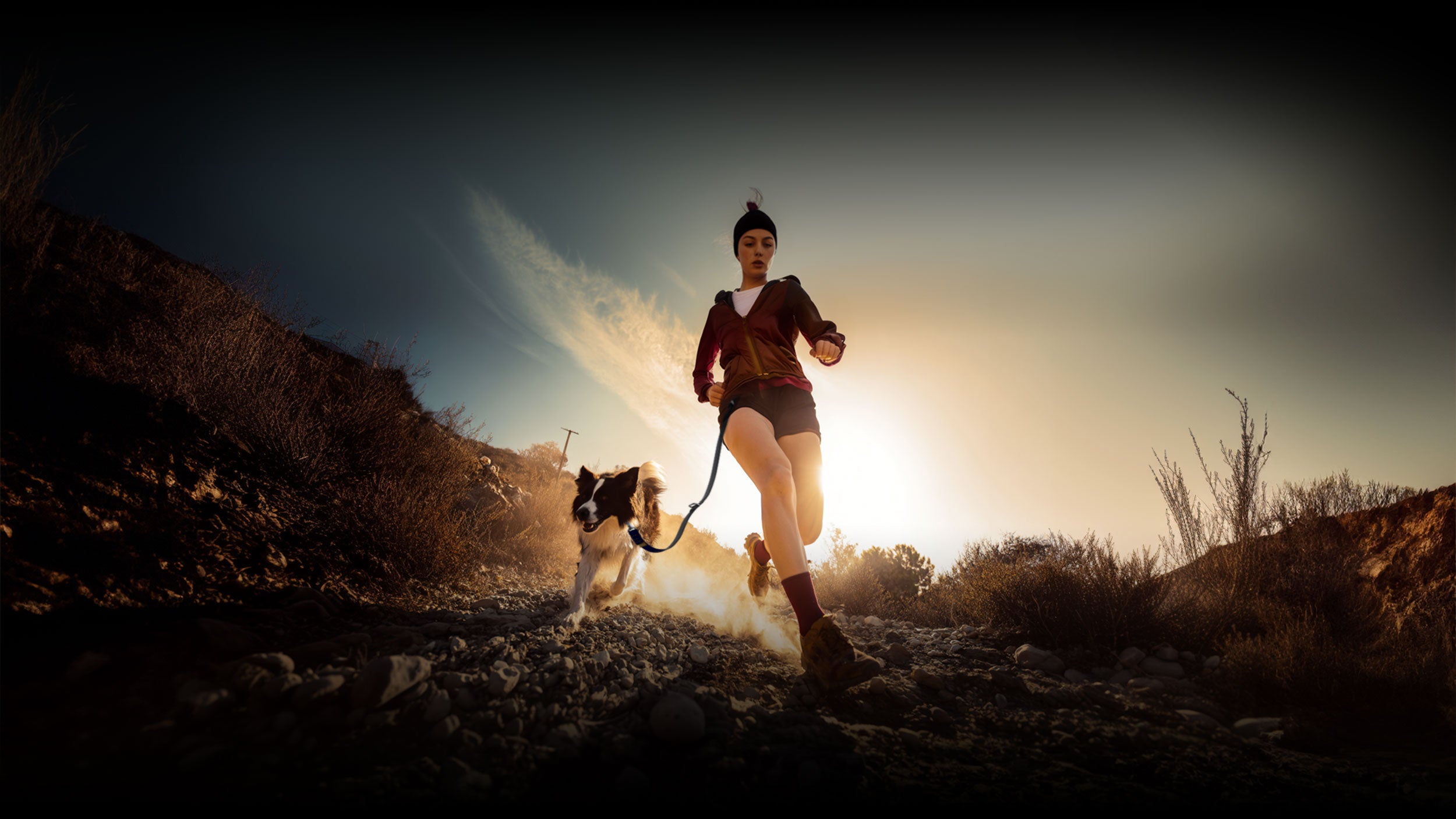 Woman running with a dog on a trail at sunset