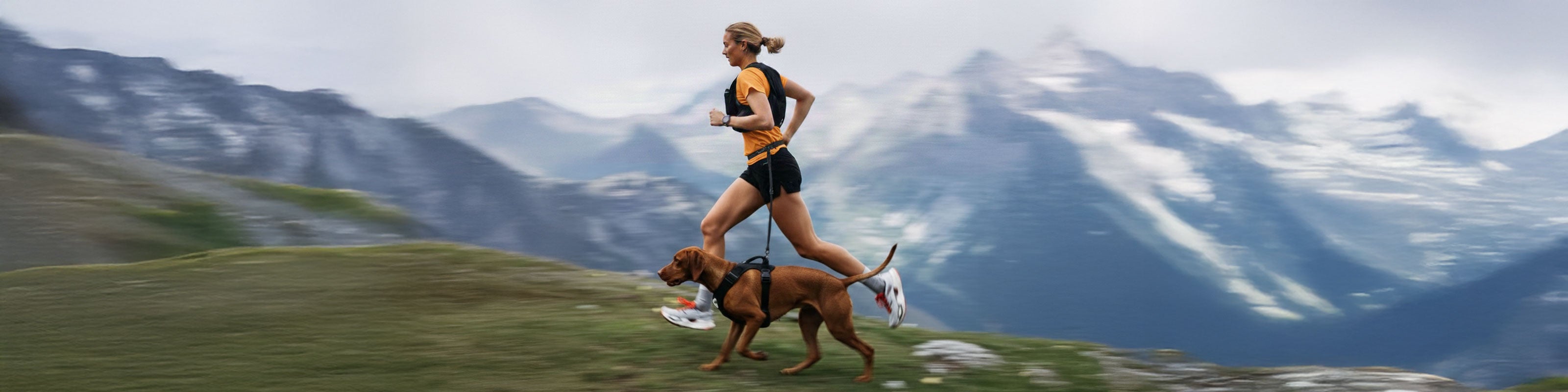 Woman running with a dog on a trail with mountains in the background